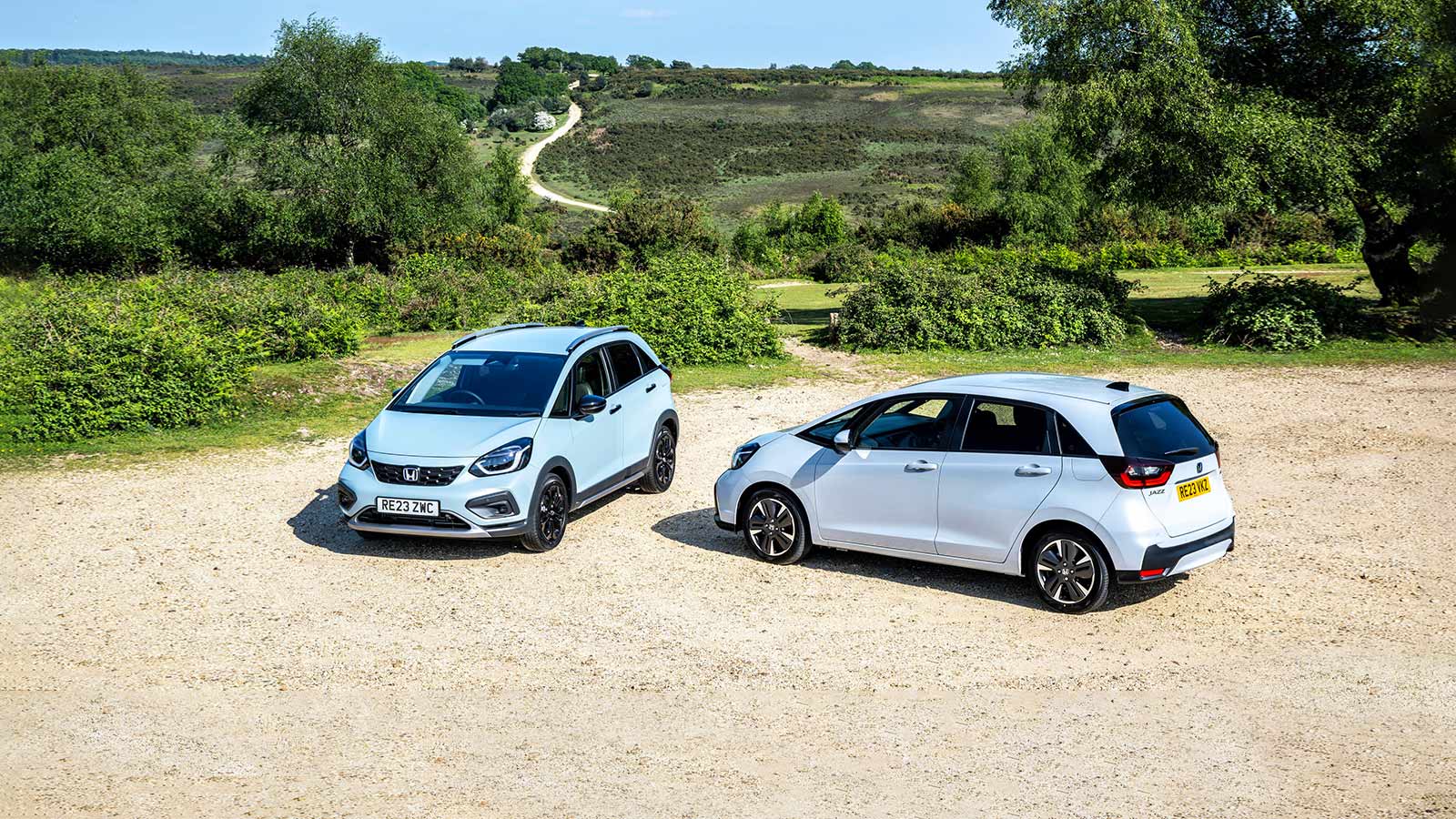 Two Honda Jazzes parked in front of a grassy landscape
