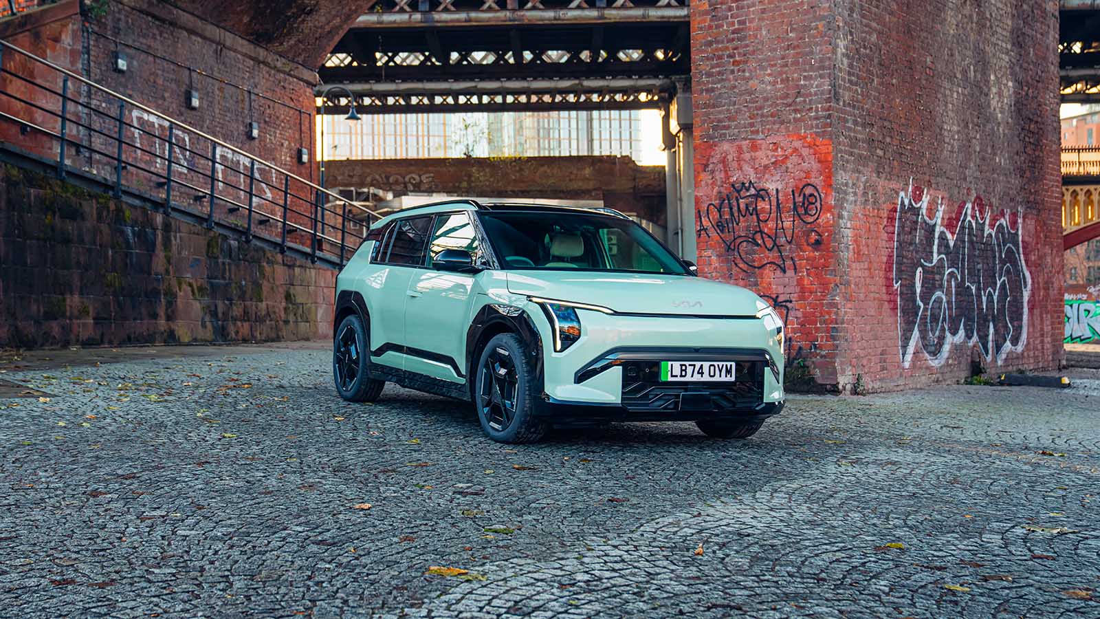 Kia EV3 in green, parked by some graffiti